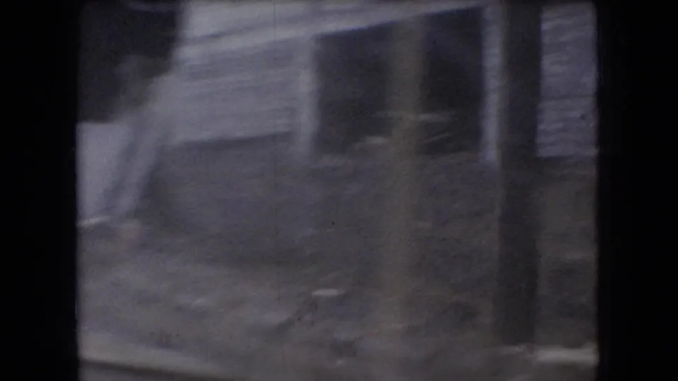 Soft, motion-blurred 8mm view of a weathered roadside wooden building in Ohio, filmed from a moving vehicle in the 1960s.