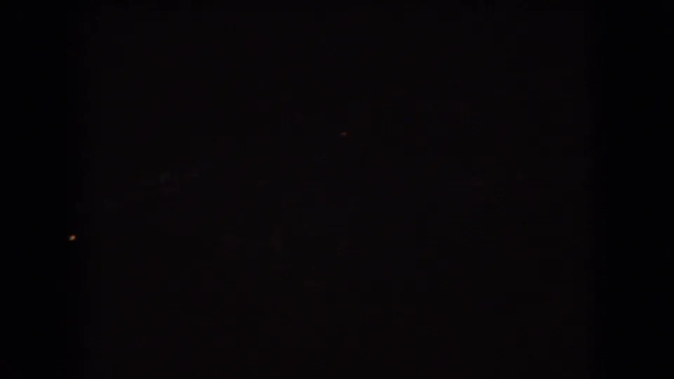 Nearly black 8mm frame with faint distant lights, likely a low-exposure nighttime or vehicle-interior moment from the Ohio travel sequence.