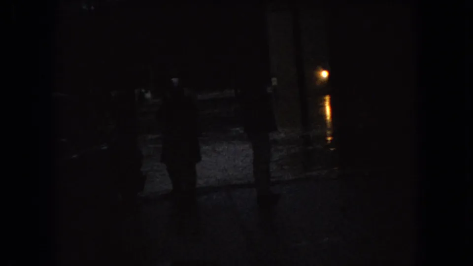 Low-light 1966 Ohio street view with silhouetted pedestrians, parked cars, and street lamp reflections on wet pavement.