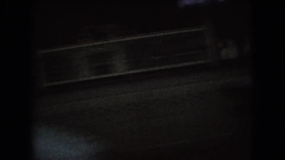 Dark 1966 Ohio 8mm frame showing wet pavement, a parked vehicle edge or curb area, and faint reflections from nearby street lighting.