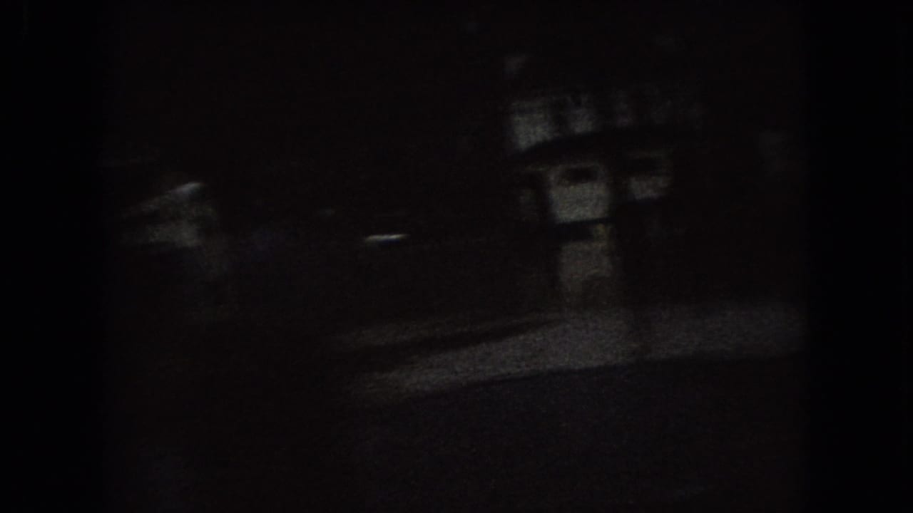 Very dark street scene with faint building shapes and a road surface.