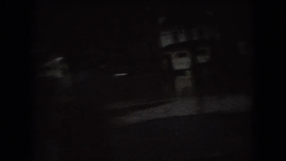 Very dark 1966 Ohio frame showing faint building forms beside a street or road, with most detail obscured by shadow and grain.