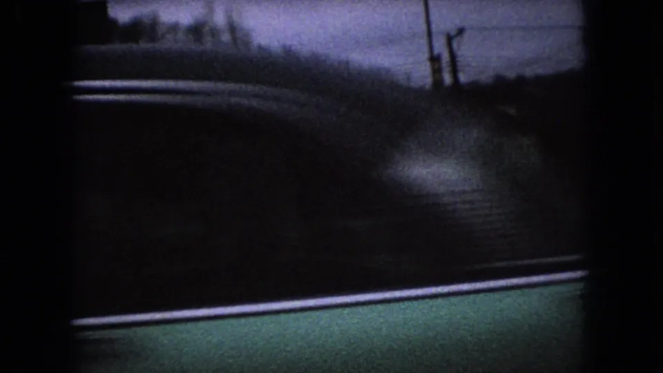 Twilight 1966 Ohio home-movie frame with utility poles and wires along a roadside, with reflective pavement or wet ground in the foreground.