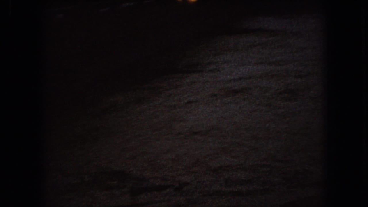 Dark murky water ripples across the frame in 1966 Ohio 8mm home-movie footage, with only faint reflected light visible near the upper edge.