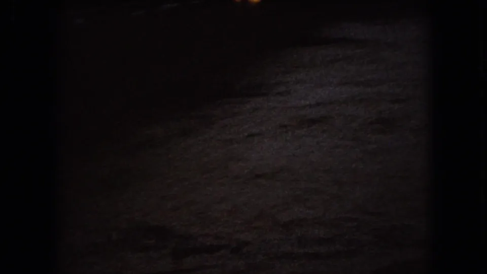 Dark murky water ripples across the frame in 1966 Ohio 8mm home-movie footage, with only faint reflected light visible near the upper edge.