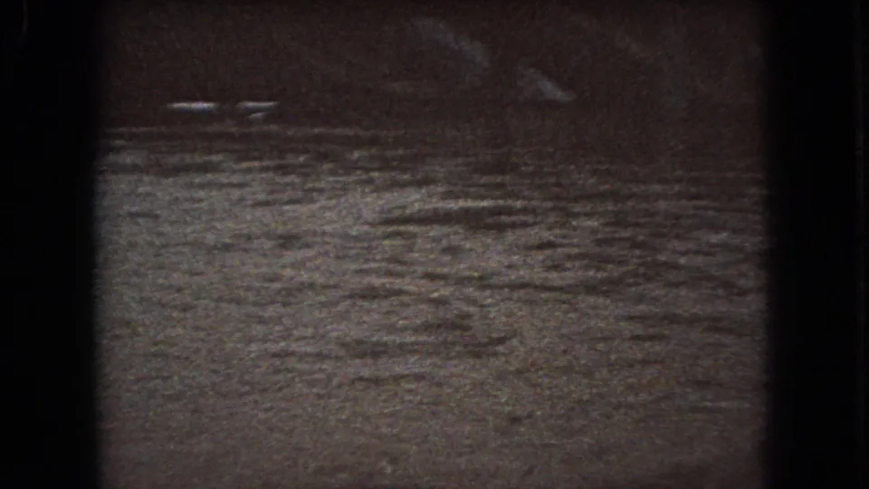 Murky moving water appears under low light in this 1966 Ohio 8mm frame, with blurred white streaks reflected across the rippling surface.