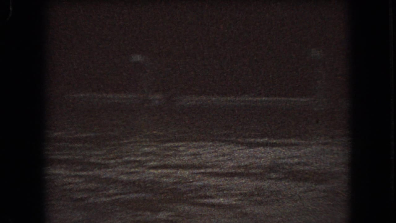 1966 Ohio 8mm frame showing a dim winter roadside or field with snow patches, a dark tree line, and heavy low-light film grain.