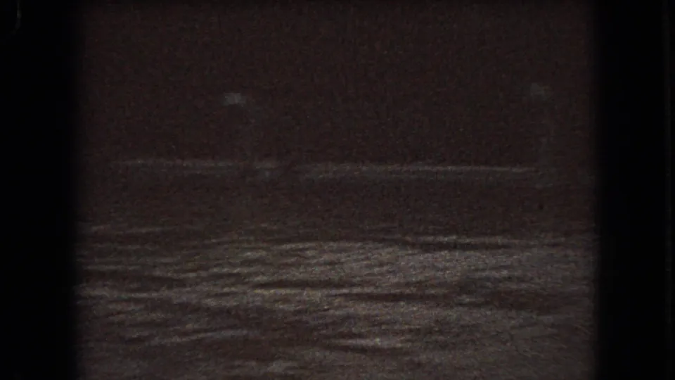1966 Ohio 8mm frame showing a dim winter roadside or field with snow patches, a dark tree line, and heavy low-light film grain.