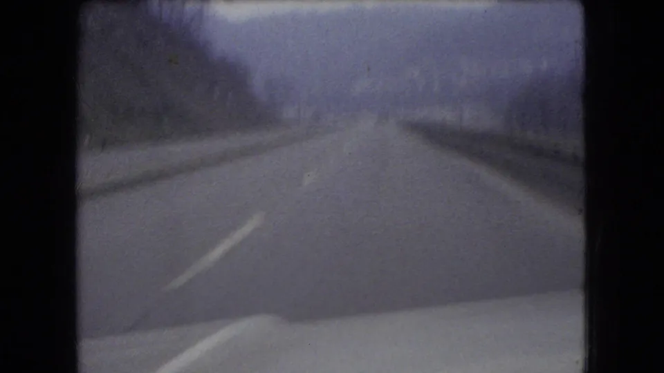 Forward-facing 1966 Ohio 8mm view of a two-lane highway through a hilly, leafless landscape from inside a moving vehicle.