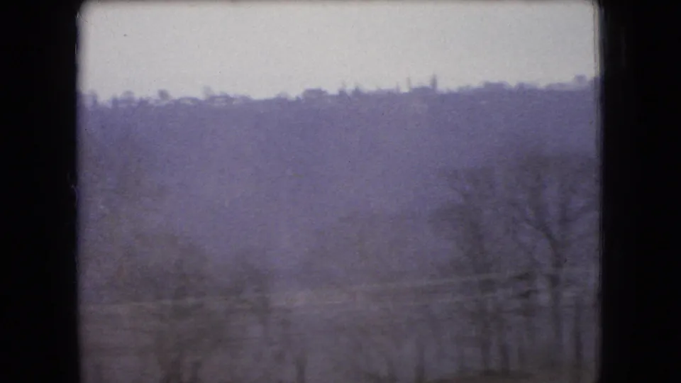 Soft 8mm view of an Ohio rural hillside with winter-bare trees in the foreground, likely filmed from a passing car.