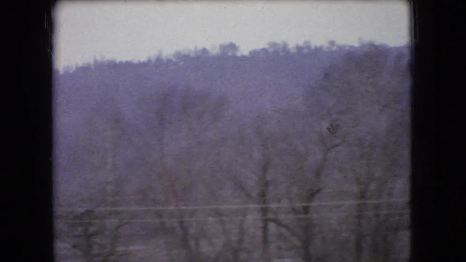Bare winter trees, a wooded hillside, and faint utility lines appear through a dark window frame in 1966 Ohio home-movie footage.