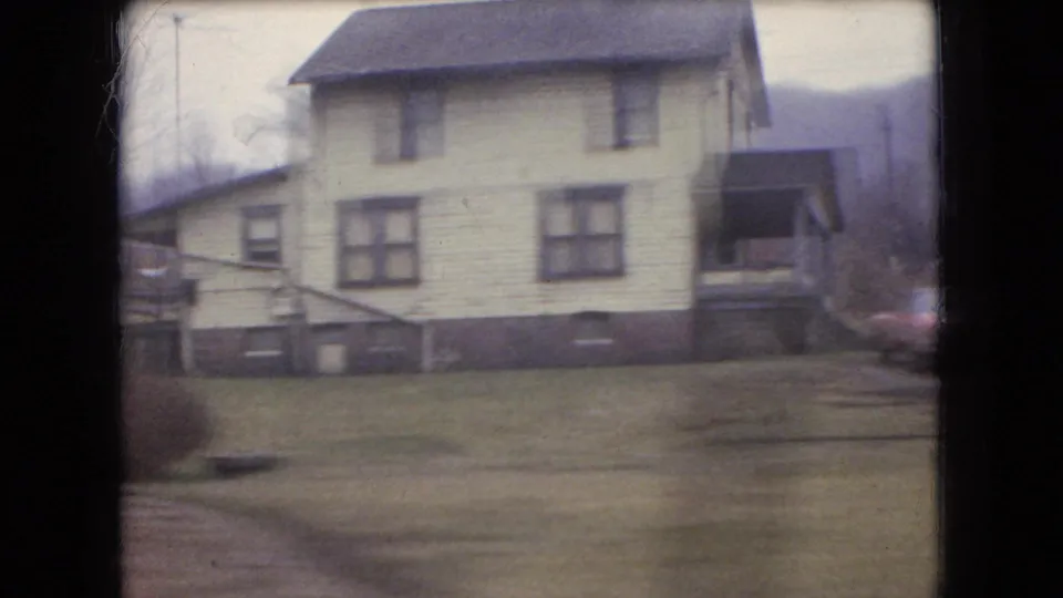 A light-colored two-story house, lawn, utility pole, and distant hillside appear in the passing 1966 Ohio roadside view.