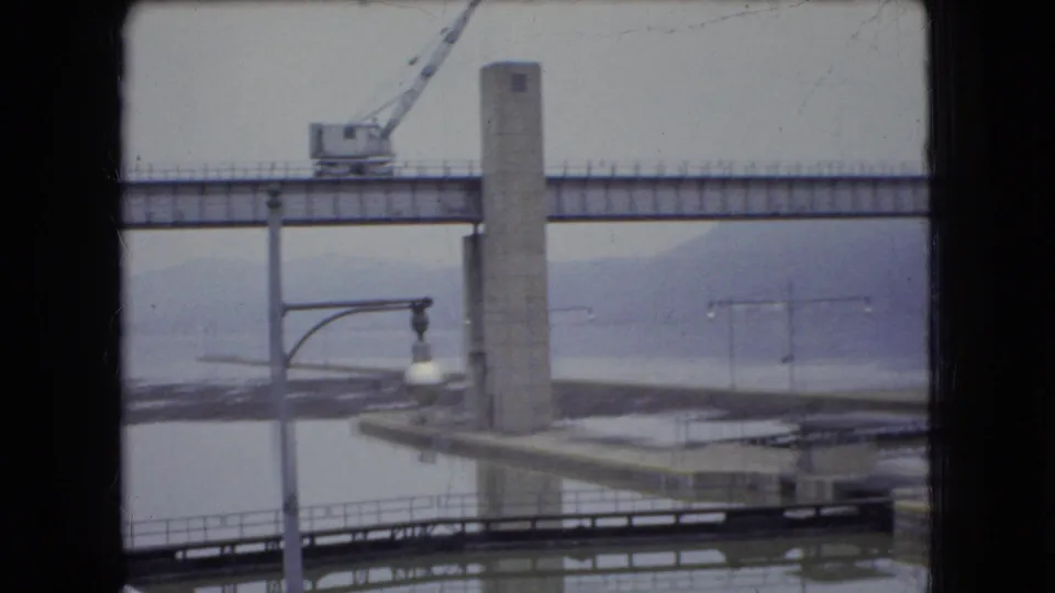 Later 1966 Ohio frame of the same bridge construction scene, with the concrete support and crane held between dark vertical frame edges.