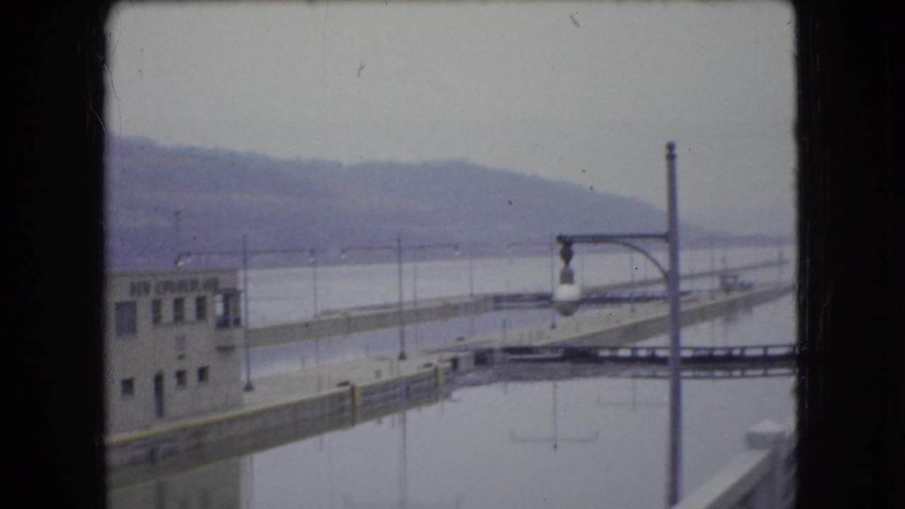 Dock structure with control building, water, lamp post, and distant hills.