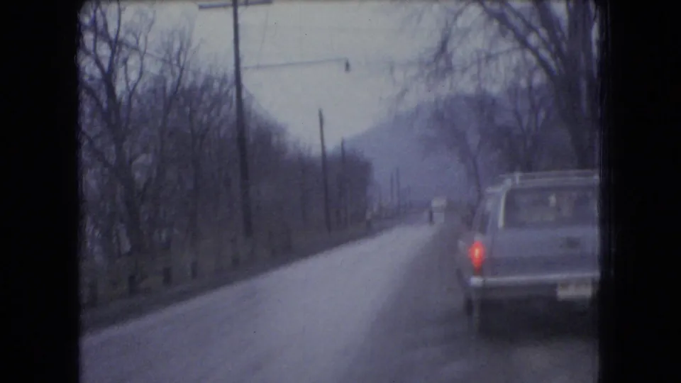The camera follows or passes a car on a rural Ohio road, with bare trees, utility poles, and a muted overcast landscape visible in the 1966 8mm frame.