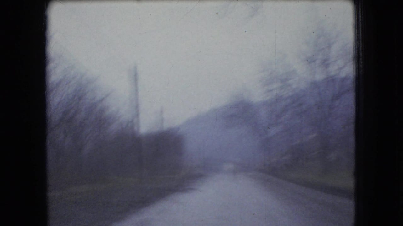 Soft 8mm view down a rural road with bare trees and hills in the distance.