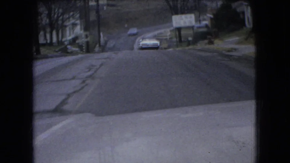 A mid-1960s car approaches on a wet, icy Ohio residential road, with a vehicle hood or dashboard visible at the bottom of the frame.
