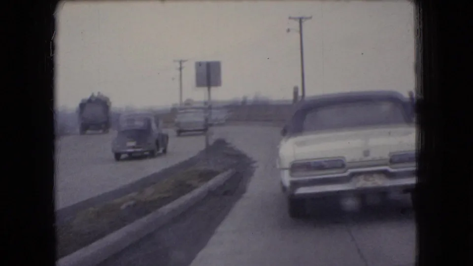 1966 Ohio 8mm frame showing a white convertible followed by other period cars on a two-lane road with utility poles and a roadside sign.