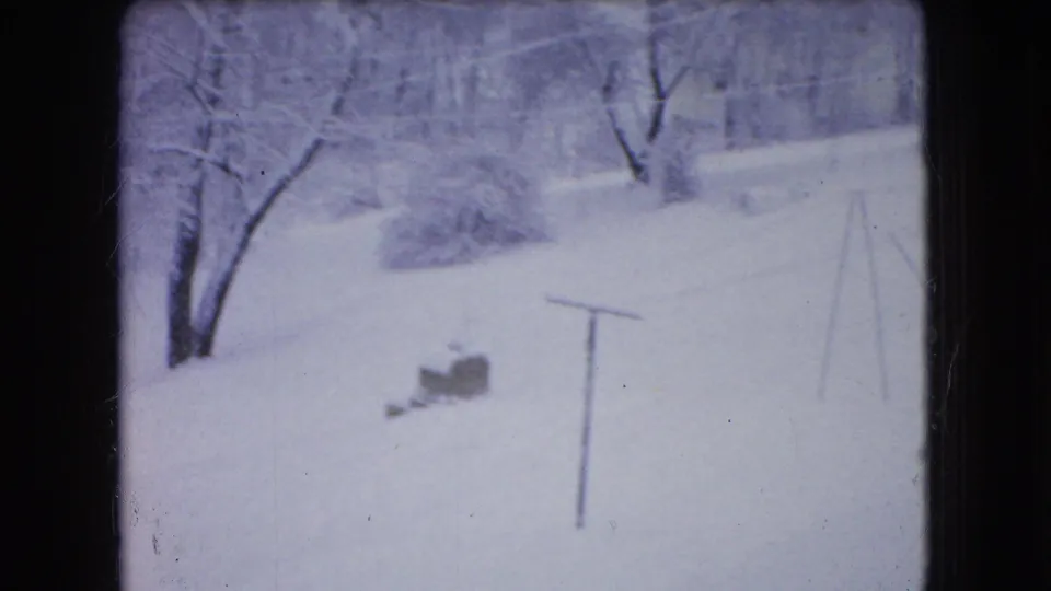 A snowy Ohio winter scene shows bare trees, white ground cover, a small brick object, and a slender pole or frame, captured in soft 8mm color.