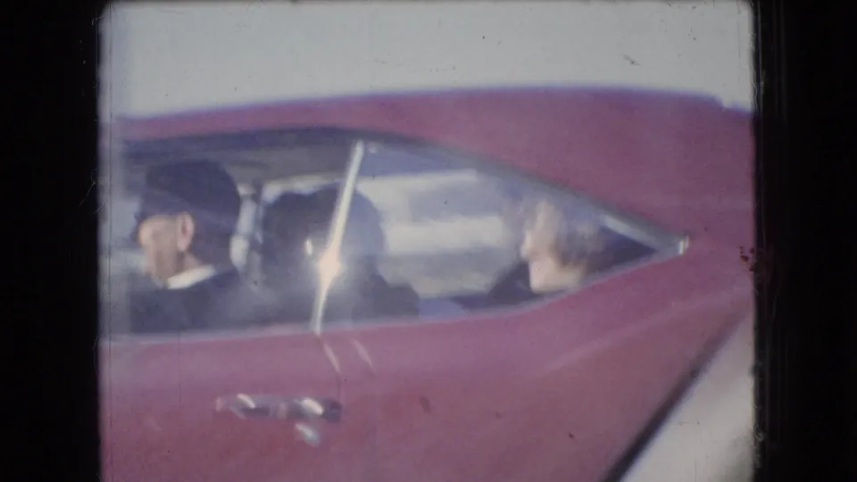 1966 Ohio home-movie frame showing the side of a red car with an adult driver and another adult occupant visible through the windows.