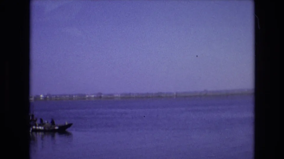 1972 Portugal 8mm frame where the small boat has moved partly out of view at the left edge, leaving calm water and a distant shoreline across the frame.