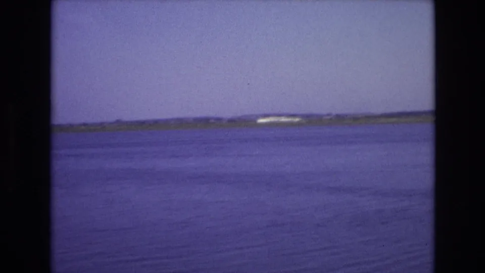1972 Portugal home-movie frame showing calm coastal water stretching toward a low distant shoreline under a pale sky.