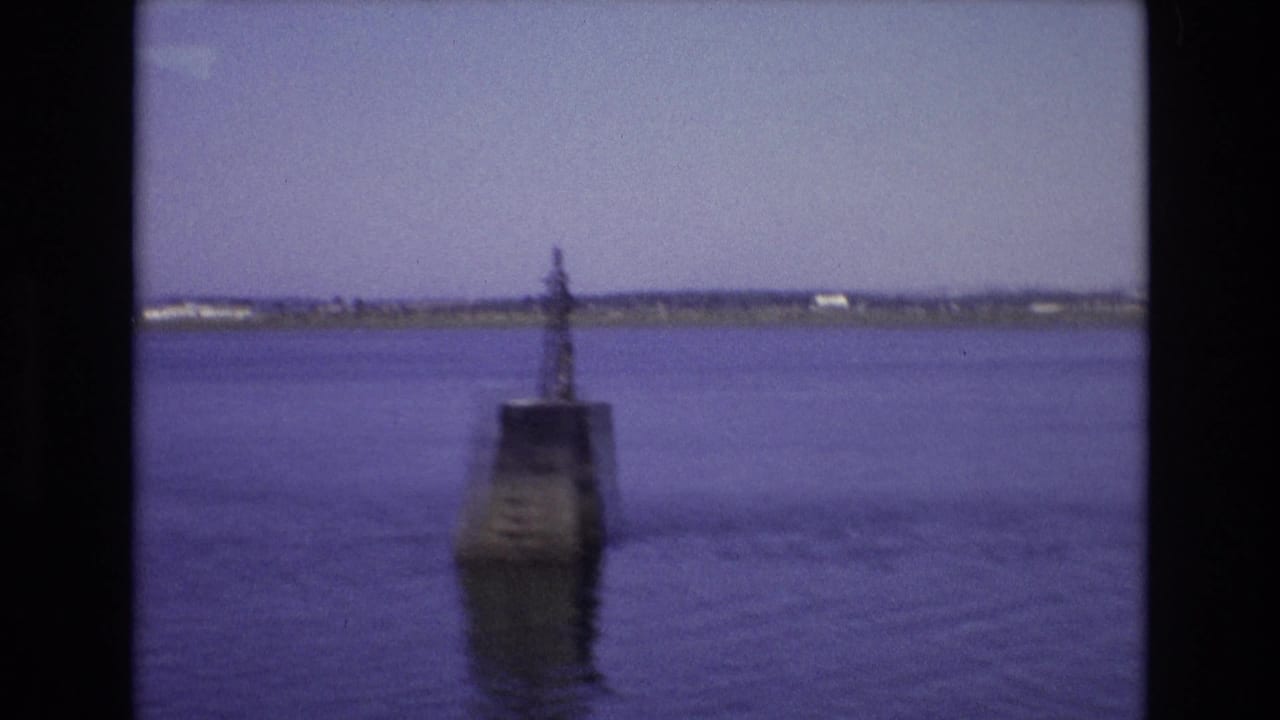 Concrete navigation marker standing in calm water with a distant shore behind it.