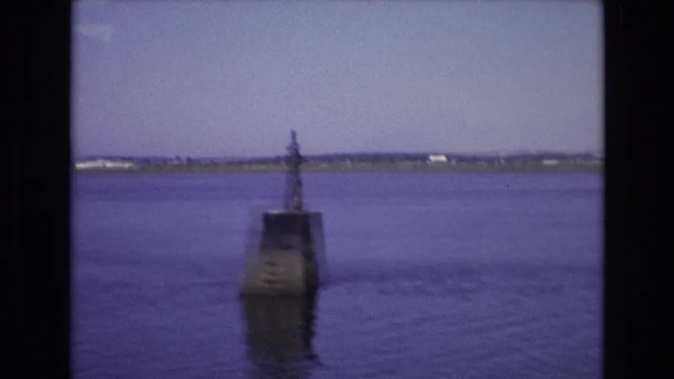 1972 Portugal coastal view with a concrete navigation marker in the water and a low shoreline in the background.