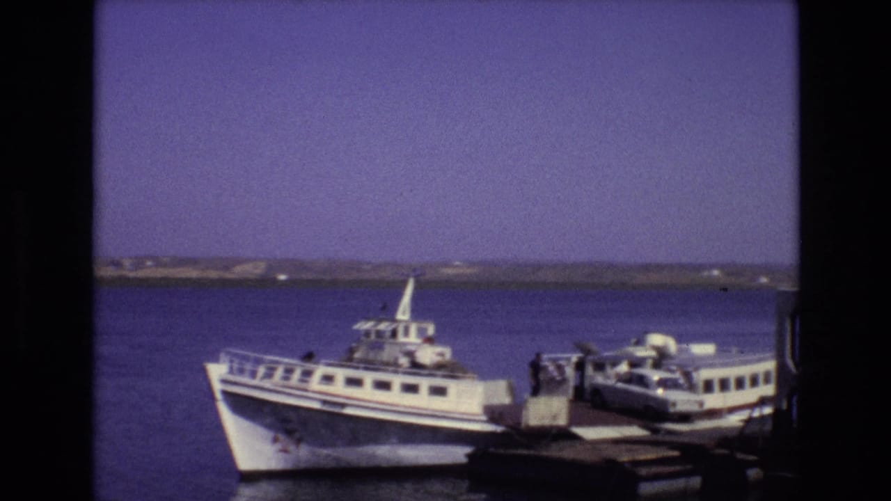 Portugal 1972 ferry scene with a white passenger vessel at a dock, a small car near the loading platform, and calm water behind it.
