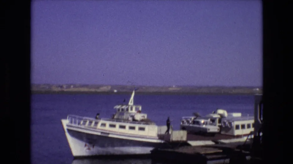 Portugal 1972 8mm frame showing a ferry moored at a waterfront platform while a compact car sits near the loading area and people stand nearby.