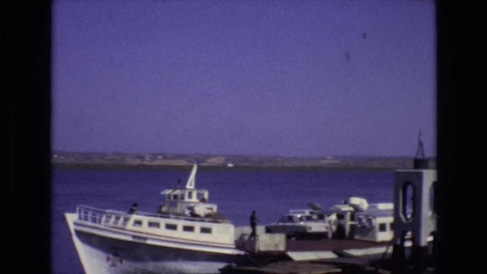 1972 Portugal 8mm frame showing a white passenger ferry at a waterfront dock, with a light-colored car and people visible near the pier.
