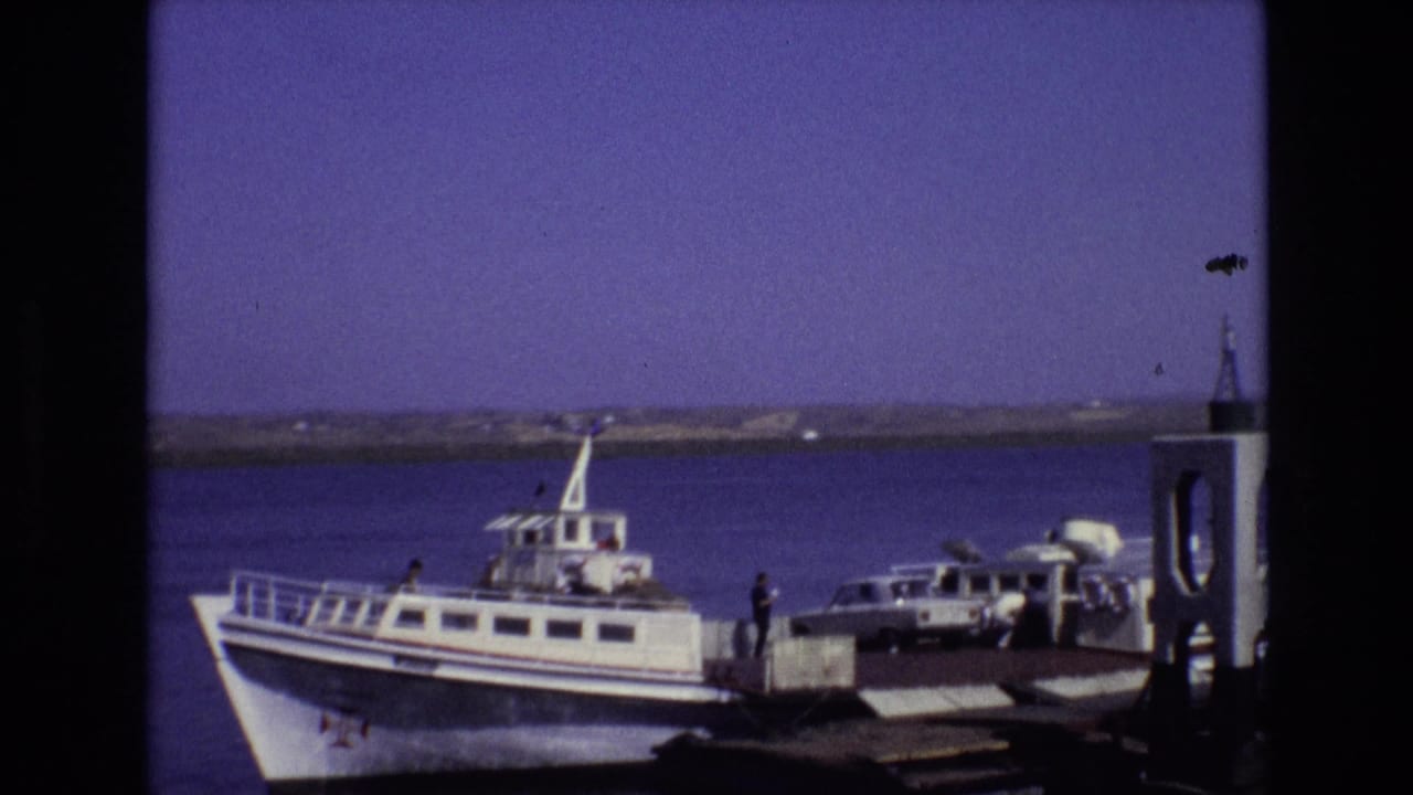 Passenger ferry moored at a dock with a car and several people beside it.