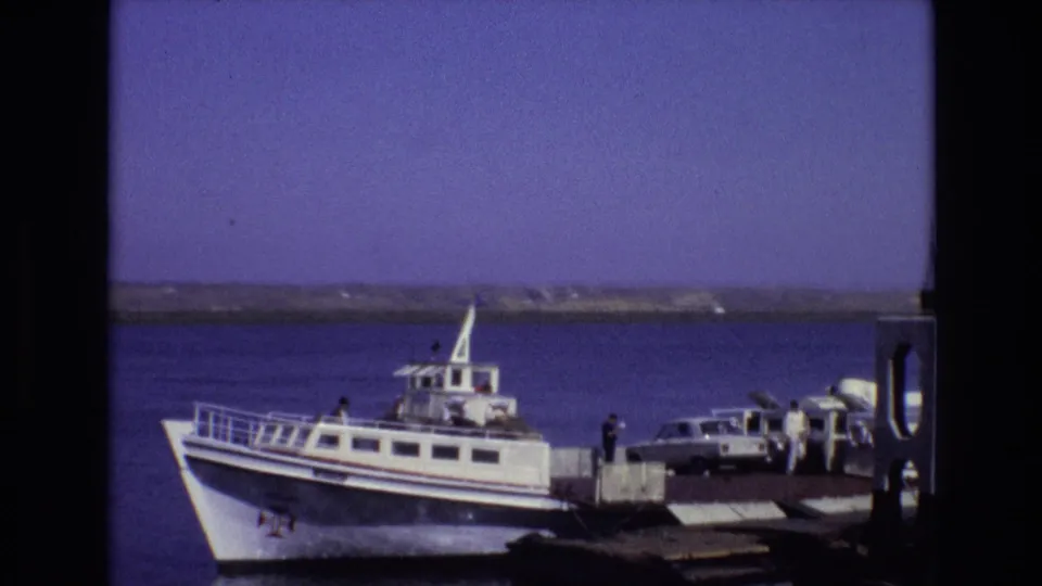 1972 Portugal 8mm still of a white ferry at a waterfront pier, with passengers or dockside figures and a light-colored car beside the boat.