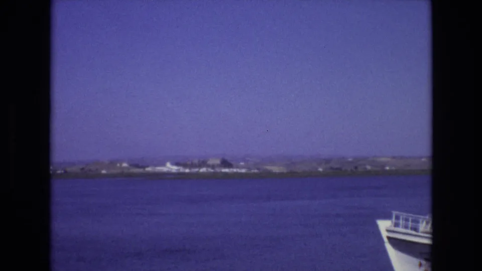 1972 Portugal coastal frame showing calm water and a distant shoreline, with the front of the ferry partly visible at the right edge.