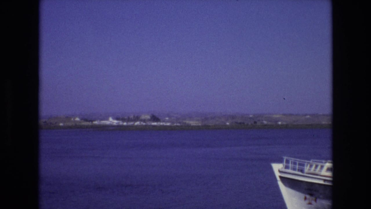 Portugal travel footage from 1972 shows calm blue water, a low distant shoreline, and part of a white boat bow in the foreground.