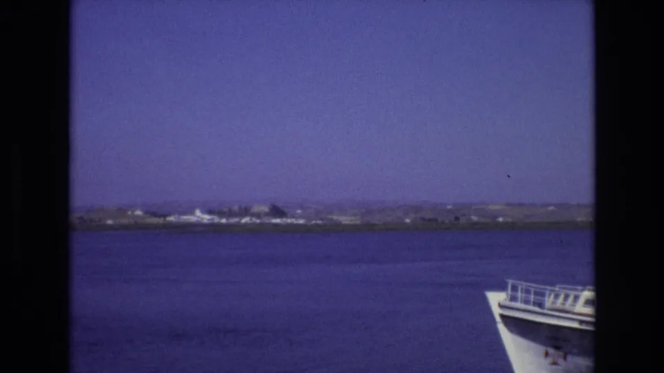 Portugal travel footage from 1972 shows calm blue water, a low distant shoreline, and part of a white boat bow in the foreground.