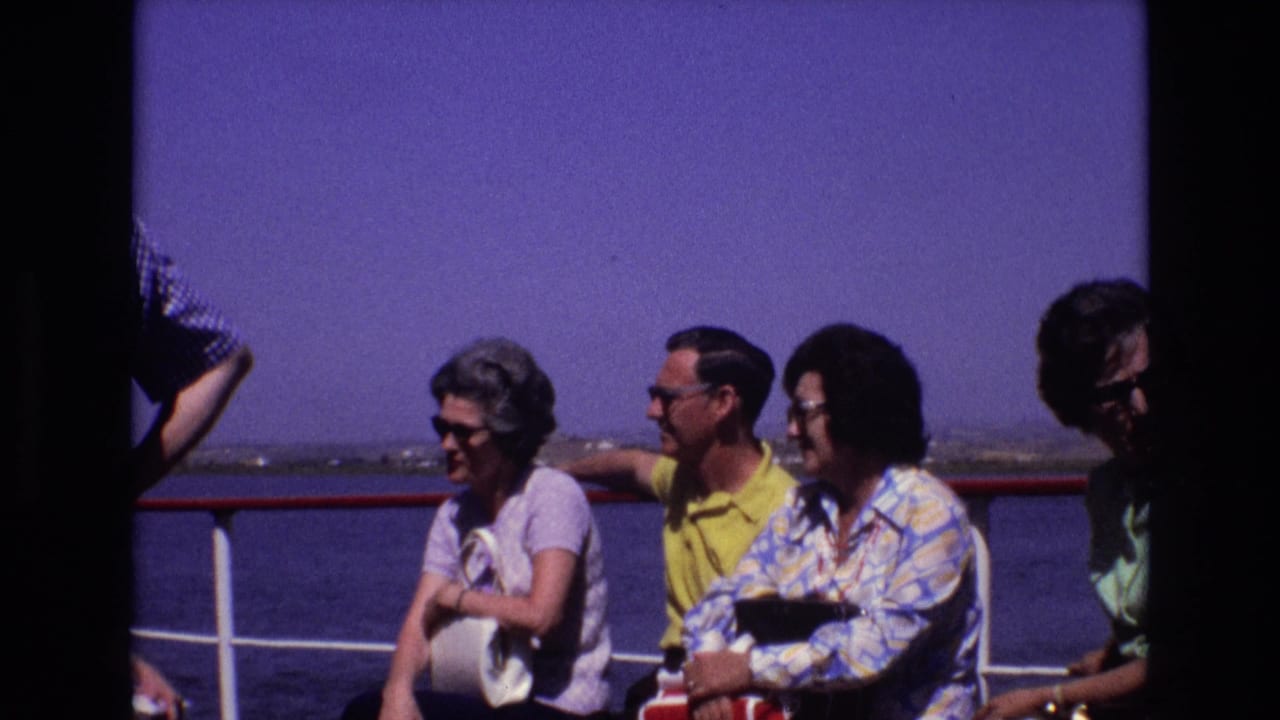 1972 Portugal home-movie frame showing adult passengers in sunglasses seated near a red-and-white ship railing with open water behind them.