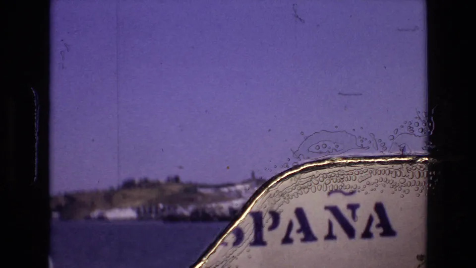 1972 Portugal 8mm frame with a soft coastal hillside across water and a prominent physical-film artifact over partial printed lettering at the right edge.