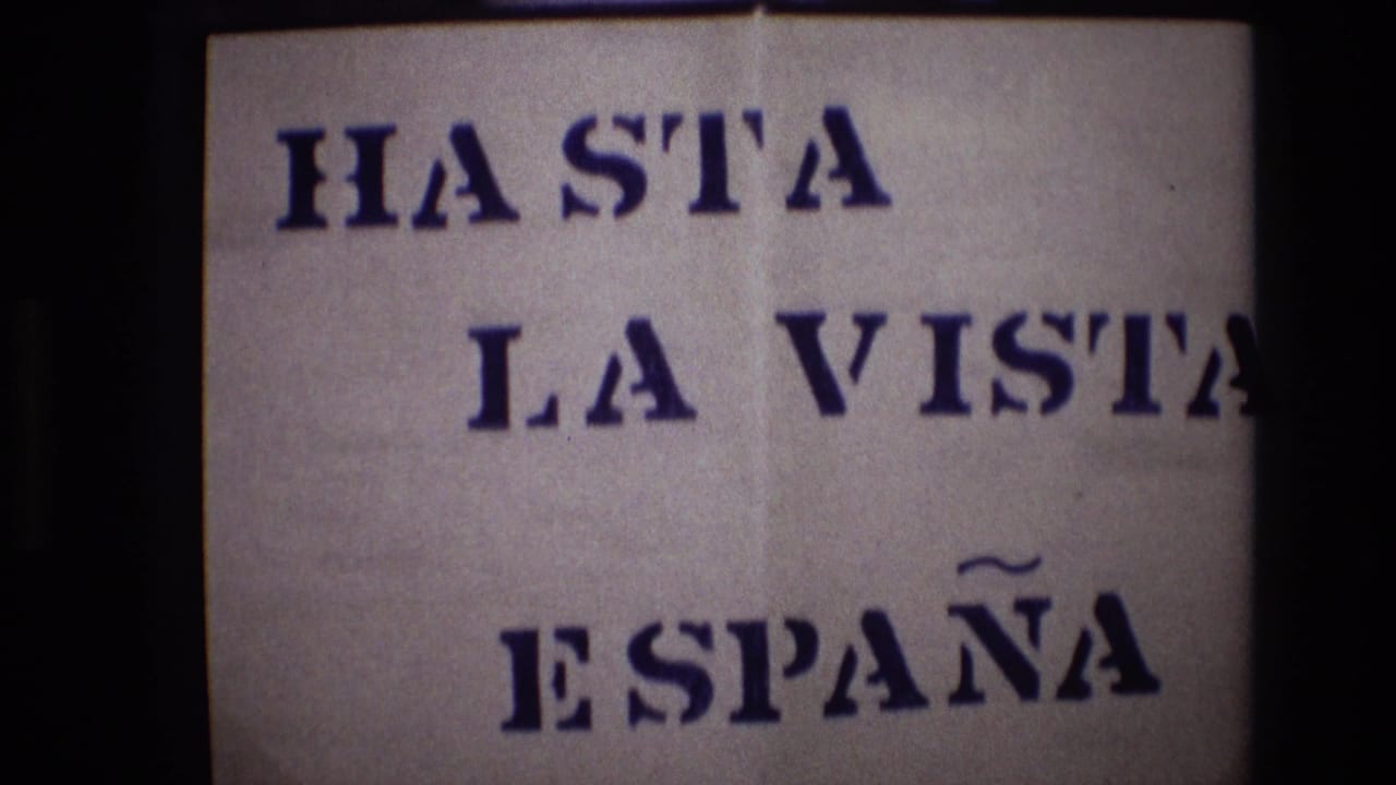 Portugal 1972 8mm frame showing an off-white handmade sign with blue stenciled text reading “HASTA LA VISTA ESPAÑA,” partly framed by dark film borders.