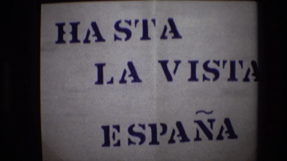 Portugal 1972 8mm frame showing the same off-white sign with blue stenciled wording, slight frame shift, and visible dark film borders.
