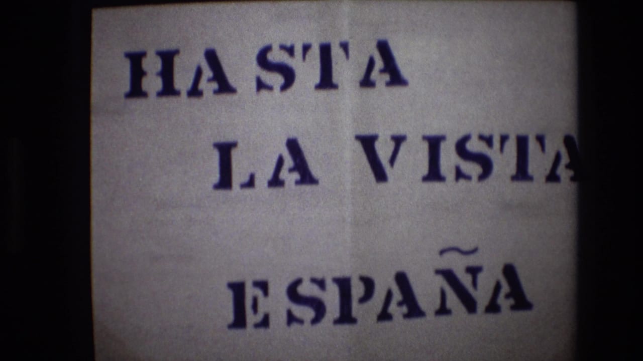 1972 Portugal home-movie frame showing a white paper sign with bold blue stencil text reading HASTA LA VISTA ESPAÑA, bordered by dark 8mm frame edges.