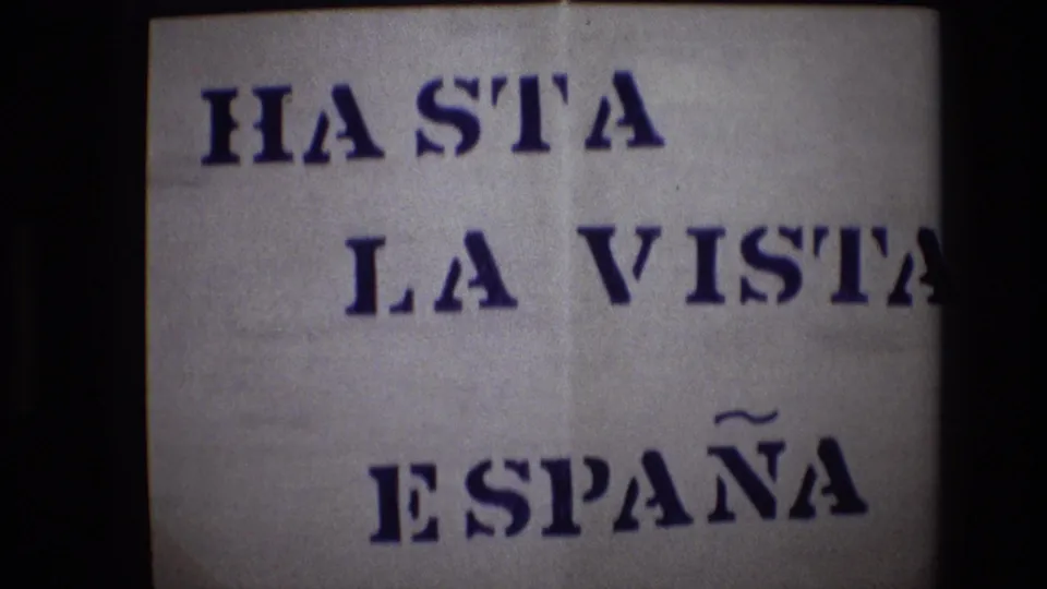 A 1972 Portugal 8mm frame centers the stenciled Spanish farewell HASTA LA VISTA ESPAÑA on creased white paper with soft focus and dark borders.