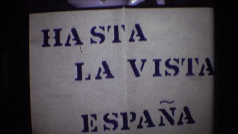 The 1972 home-movie frame shows the same hand-stenciled HASTA LA VISTA ESPAÑA sign shifted lower in the 8mm gate, with visible paper texture and dark edging.