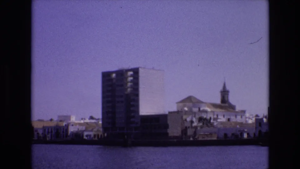Final 1972 Portugal frame showing the same waterfront grouping of a tall building, white structures, and a steeple across the water with visible film color shift.
