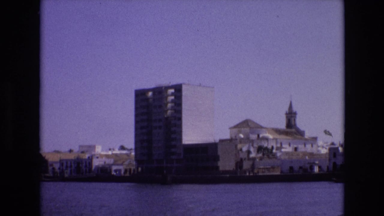 1972 Portugal 8mm frame looking across a waterway toward a modern high-rise beside white waterfront buildings and a church steeple.