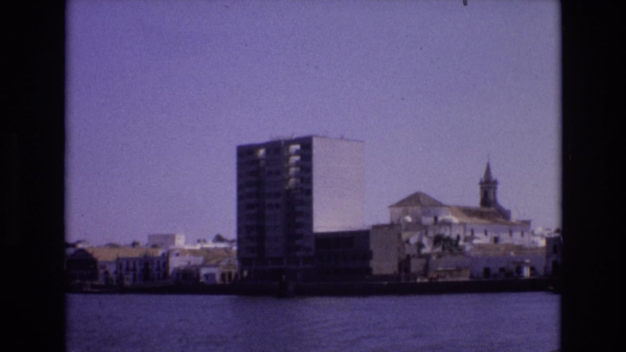 Across-water view of a high-rise, white buildings, and a church steeple under a purple-tinted sky.