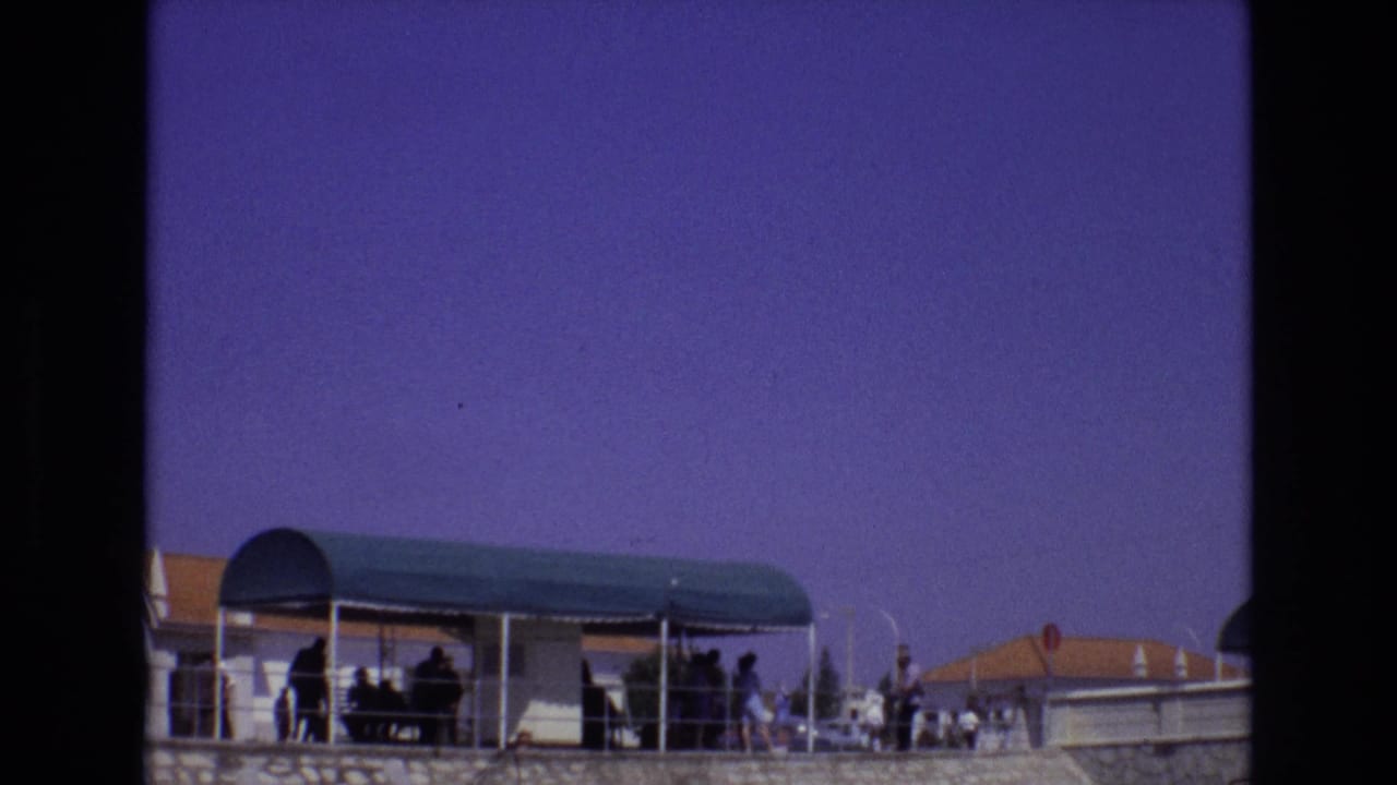 Canopy and terrace with small figures standing near railings and rooftops in the background.