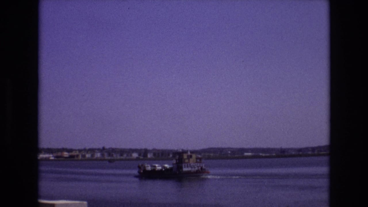 1972 Portugal 8mm frame of a small commercial-looking boat traveling across a broad waterway beneath a purple-tinted sky.