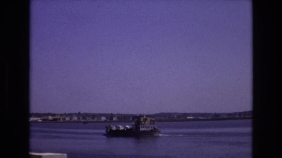 1972 Portugal 8mm frame of a small commercial-looking boat traveling across a broad waterway beneath a purple-tinted sky.