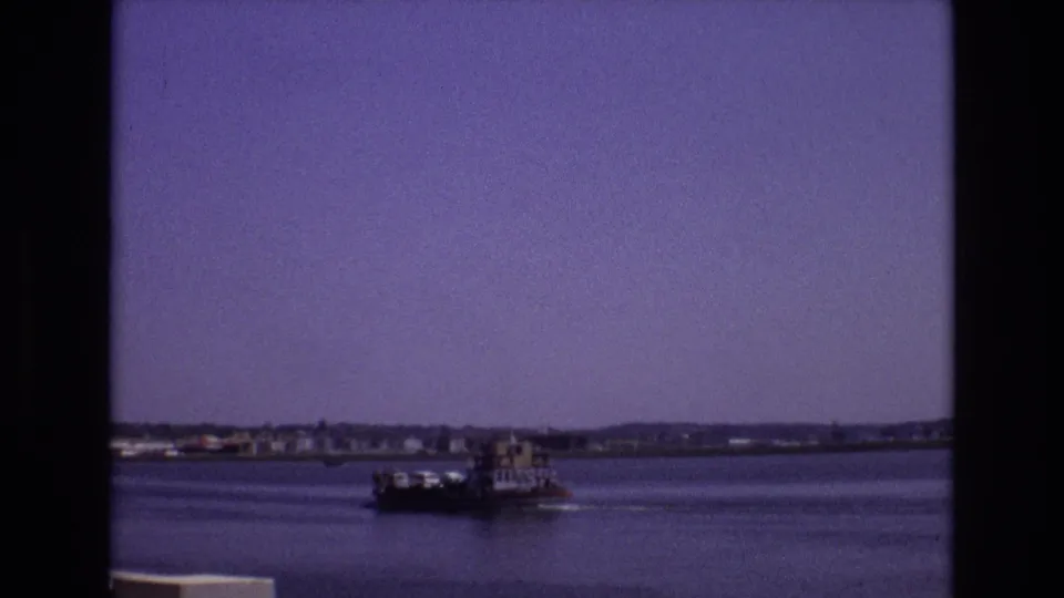 1972 Portugal 8mm frame showing a small riverboat near the lower part of the view, with calm water, distant shore, and dark frame edges suggesting a window or doorway viewpoint.